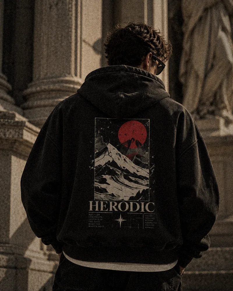 Model from behind in a washed black HERODIC hoodie with the Crimson Summit back print: a red sun over snowy peaks